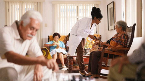 Una dona atèn una altra a una habitació amb gent gran