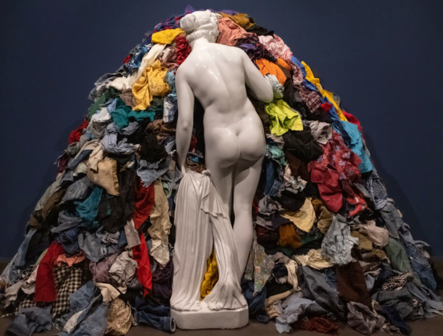 Escultura deessa grega recolzada en una pila gegant de roba